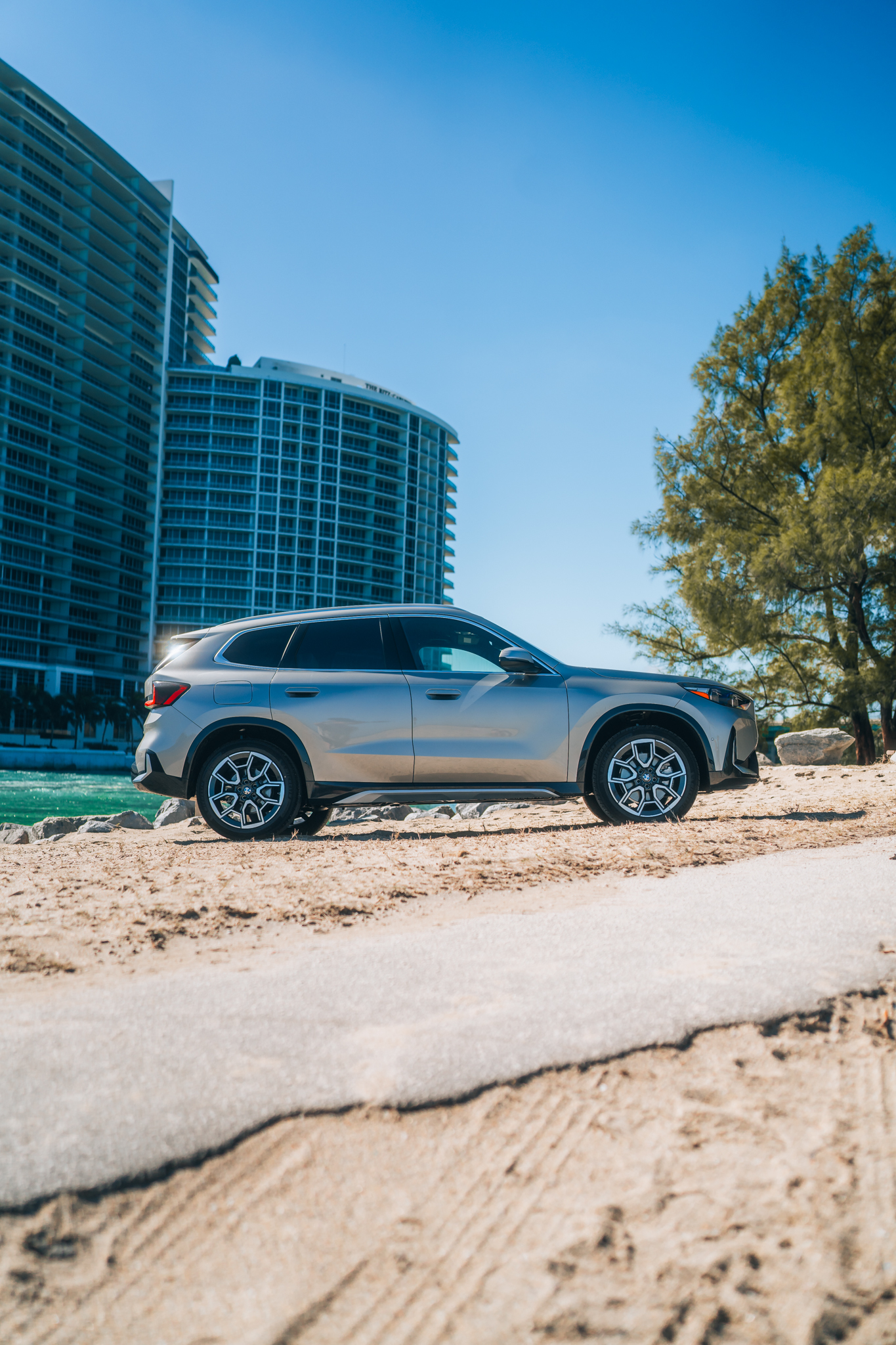 BMW X1 xDrive28i side profile — palm tree and coastal rocks
